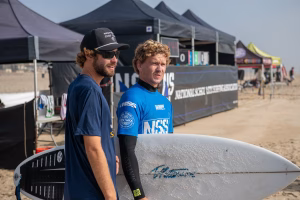 Westcliff Warriors Surf Team celebrating victory at Huntington Beach Pier after NSSA college surf competition, holding boards with Pacific waves in the background.