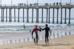 Westcliff Warriors Surf Team celebrating victory at Huntington Beach Pier after NSSA college surf competition, holding boards with Pacific waves in the background.